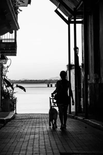 black and white photo of street towards the sea with girl walkin