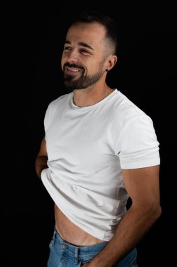 Stüdyoda gülümseyen bir adam beyaz tişört kaldırıyor.