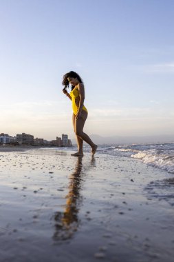 Latin, kumsalda poz veriyor. Sarı mayo giyiyor.