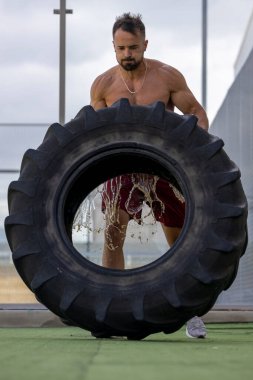 Güçlü üstsüz bir adam kamyon tekerleğiyle çaprazlama yapıyor..