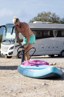 Sörfçü sörf tahtasını şişiriyor.