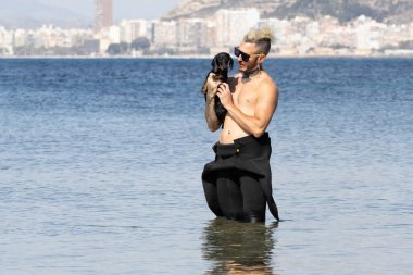 Kumsalda köpeğini tutan bir adam.