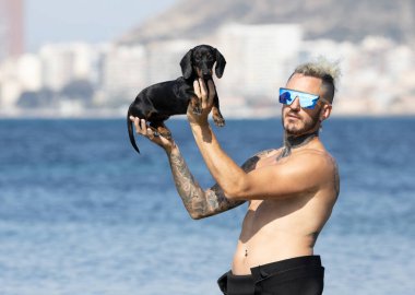 Kumsalda köpeğini tutan bir adam.