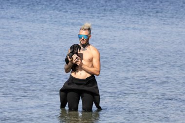 Kumsalda köpeğini tutan bir adam.