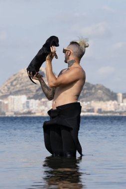 Kumsalda köpeğini tutan bir adam.