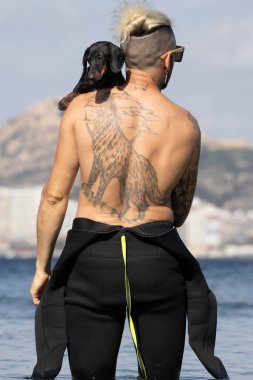 Kumsalda köpeğini tutan bir adam.