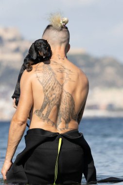 Kumsalda köpeğini tutan bir adam.