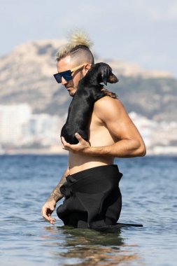 Kumsalda köpeğini tutan bir adam.