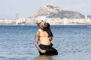 Kumsalda köpeğini tutan bir adam.