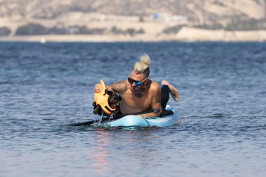 Kürek tahtasındaki adam köpeği sudan çıkarıyor..