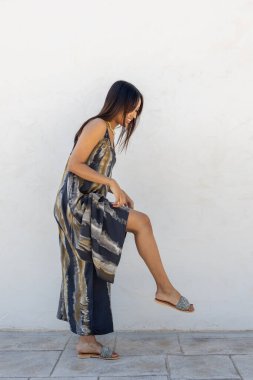 Beyaz bir duvara karşı yazlık elbiseyle poz veren Kolombiyalı bir model.