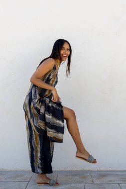 Beyaz bir duvara karşı yazlık elbiseyle poz veren Kolombiyalı bir model.