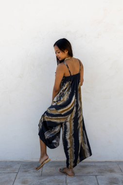 Beyaz bir duvara karşı yazlık elbiseyle poz veren Kolombiyalı bir model.