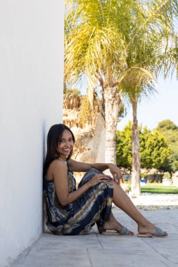 Esmer kadın yerde oturuyor ve yaz kıyafetleriyle poz veriyor..