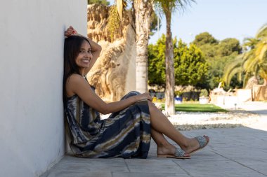 Esmer kadın yerde oturuyor ve yaz kıyafetleriyle poz veriyor..