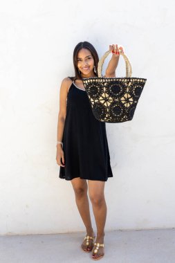 Siyah elbiseli Kolombiyalı manken yaz çantasını gösteriyor..