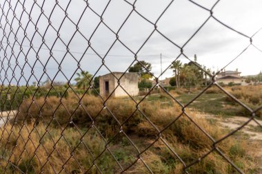 Su damlaları olan demir bir çitin arkasında terk edilmiş bir ev..