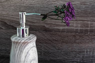 a light gray liquid soap container with a silver dispenser with purple flower in it on wooden background. Useful hygiene products and personal are. Place for texting or logo