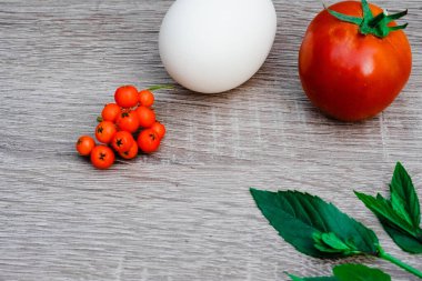 still life of fresh red one tomato and one egg, mint, berries for the salad on a wooden background, close up. Healthy eating concept. Place for text or logo