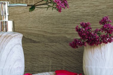 a light gray liquid soap container with a silver dispenser and with pink rose petals on wooden background. Useful hygiene products and personal care. Place for texting or logo