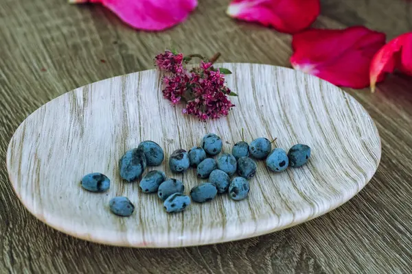 a soap dish with petals of pink rose, blue bilberries, purple lilac on wooden background. Useful hygiene products and personal care. Place for texting or logo