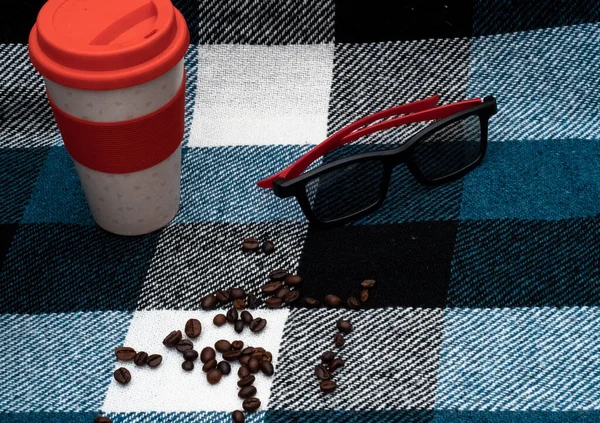a cup of coffee with a checkered plaid and sunglasses on a gray background.