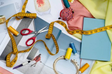 Kırmızı makas, ölçüm bantları ve sarı ve pembe kumaş üzerinde mavi ve beyaz plastik bardak yakın çekim