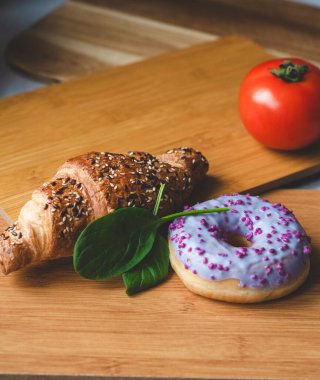 Bir taze kruvasan, bir lezzetli çörek, iki yeşil nane yaprağı ve bir olgun kırmızı domates. Eski ahşap tepsilerde taze ve aromatik kahvaltı.