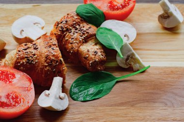 İki adet taze pişmiş kruvasan, mantar, nane ve olgun domatesli kahverengi tahta. Fırın kavramı