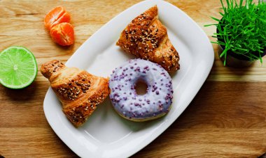 one glazed violet donut, lime and resh juicy mandarin slices on white ceramic plate on wooden board. Healthy food concept clipart