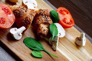 İki adet taze pişmiş kruvasan, mantar, nane ve olgun domatesli kahverengi tahta. Fırın kavramı