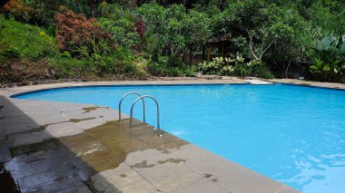 Açık yüzme havuzu ağaçların arasında. İçinde bir çocuk yüzüyor..