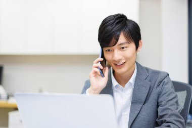 Genç Japon işadamı ofiste çalışırken telefonla konuşuyor..
