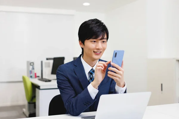 年轻的日本商人在办公室用他的电话 — 图库照片