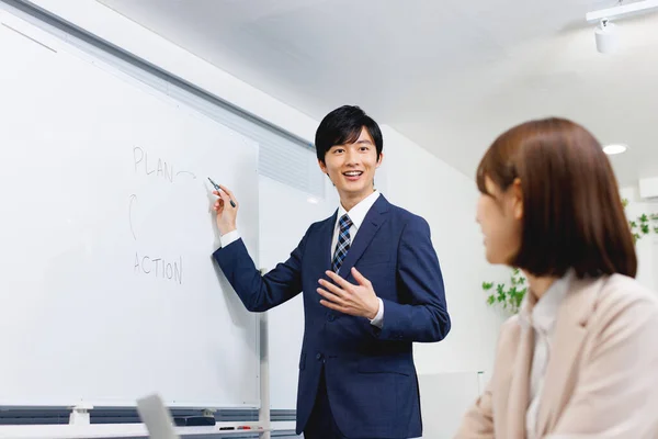 オフィスの若い日本人男性が女性同僚にビジネスプランを提示 — ストック写真