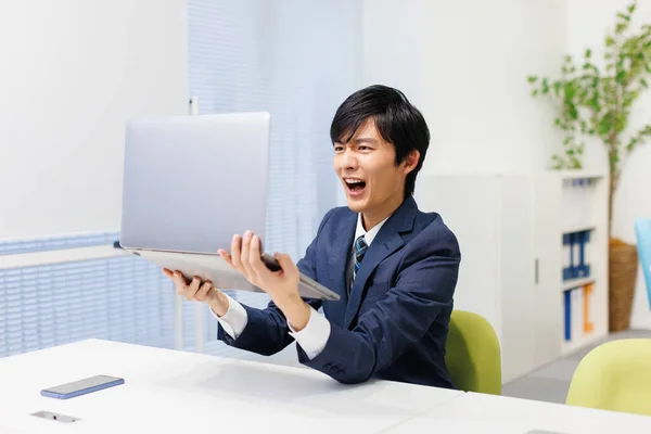 Mladý Japonský Muž Šokován Při Držení Svého Notebooku Kanceláři — Stock fotografie