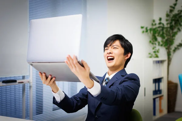 Mladý Japonský Muž Šokován Při Držení Svého Notebooku Kanceláři — Stock fotografie