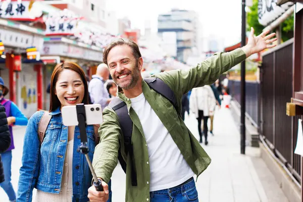 Kafkas erkek ve Japon kadın eski Japon caddesinin arka planında selfie çekiyorlar.