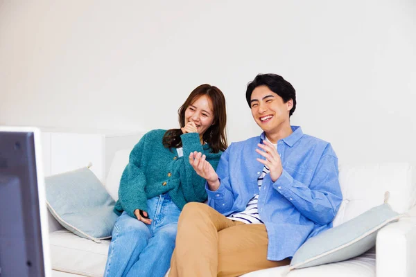 young asian couple sitting at couch with television