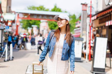 Sokakta yürüyen Japon kadın. Bagajlı çekici bayan turist şehrin cazibesine bakıyor.