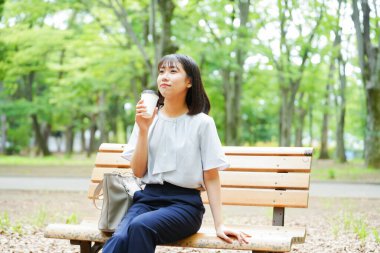 Kahve içen bir kadın parkta bankta oturuyor.