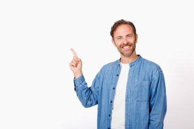 Beyaz stüdyo arkaplanını işaret eden mavi gömlekli beyaz bir adamın portresi.