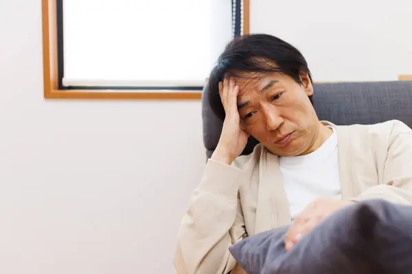 老弱病残的亚洲男人 头痛躺在沙发上 — 图库照片