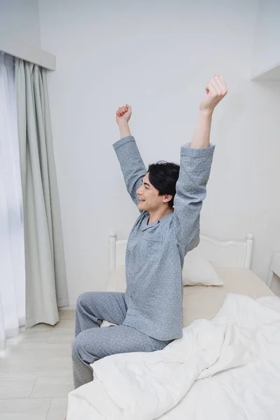 handsome asian man wearing pajamas stretching after sleep