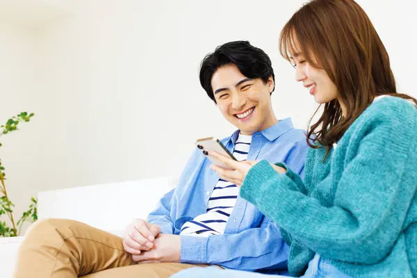 Junges Japanisches Paar Sitzt Hause Auf Couch Und Nutzt Smartphone — Stockfoto
