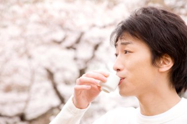 Parkta kiraz çiçekleriyle çay içen Asyalı adam.