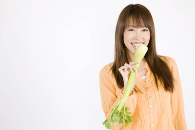 gülümseyen genç Asyalı kadın beyaz arka planda kereviz sapı yiyor.