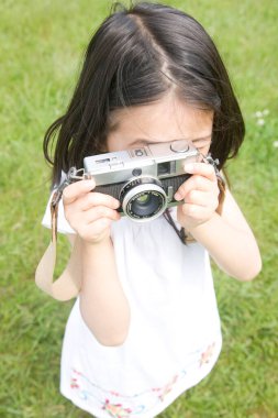 Küçük Asyalı kız dışarıda fotoğraf makinesi kullanıyor.