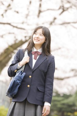 Çiçek açan kiraz ağacı arka planında poz veren güzel Japon okul kızının portresi.