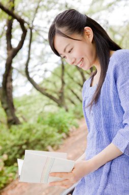 Yeşil yaz parkında gündüz kitap okuyan neşeli Japon kadın. 